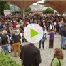 Standbild eines Videos: Viele Menschen stehen gemeinsam auf einem Platz, einige unterhalten sich oder tanzen.