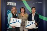 Drei Frauen stehen in einer Reihe. Die beiden links und rechts halten eine Mappe in der Hand.