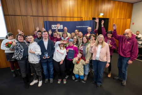 Viele Menschen stehen vor einer blauen Wand und winken