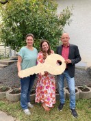Drei Personen halten einen großen Holzschlüssel in den Händen