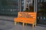 Eine orangene Sitzbank steht vor einem Fenster. Auf der Bank steht "Kein Platz für Gewalt gegen Frauen und Mädchen"