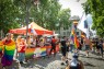 Man sieht einen Pavillon und Menschen in einem abgesperrten Bereich. Davor geht die CSD-Demo entlang. 
