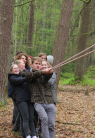 Man sieht eine Gruppe junger Menschen, die gemeinsam an einem Seil ziehen. Im Hintergrund sieht man den Wald.