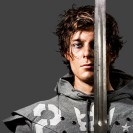 Eine männliche Person im grauen Sweatshirt mit einem langen Schwert in der Hand.