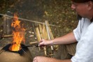 Foto: ein Mann mit Metallstäbchen über einer Feuerstelle