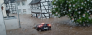 Man sieht weiße Fachwerkhäuser, die von braunen Wassermassen umspült werden. Im Wasser treibt ein schwarzes Auto, das man von hinten sieht.