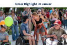 Eine blonde Frau und ein Mann mit schwarzer Kappe lächeln einander an. Der Mann sitzt im Rollstuhl. Um sie herum sieht man klatschende Menschen mit und ohne Behinderung.