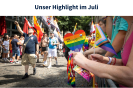 Eine Parade bunt gekleideter Menschen läuft lachend und jubelnd über eine Straße. Auf beiden Seiten stehen Menschen und schwenken Regenbogenfahnen.