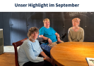 Eine Mann und eine Frau sitzen an einem Holztisch und unterhalten sich. Ein Mann mit großer Kamera filmt das Gespräch.