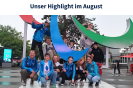 Eine Gruppe von Jugendlichen posiert hockend und stehend auf einem Podest mit der Statue des Paralympics-Symbol.