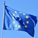 Eine blaue Europa-Flagge mit kreisförmig angeordneten gelben Sterne weht vor dem blauen Himmel.