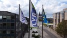 Man sieht zwei Flaggen mit dem LVR-Logo und eine Internationale Gehörlosenflagge vor der Skyline in Köln-Deutz.