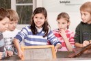 Drei Kinder stehen nebeneinander. Ein Mädchen mit braunen Haaren hält einen hölzernen Rahmen zum Papierschöpfen in den Händen.