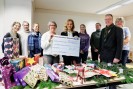 Eine Gruppe Menschen steht mit einem großen weißen Check in der Hand lächelnd vor einem Tisch mit Weihnachtsgeschenken.