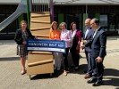 Eine Gruppe lächelnder Menschen steht auf einem Spielplatz und hält ein großes Schild mit der Aufschrift: "Nach Hochwasser: Initiative für den Wiederaufbau Handwerk baut auf!"