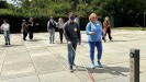 Man sieht eine Gruppe von menschen in Zweier-Paaren auf einem Museumsvorplatz entlang gehen. Eine der Personen trägt jeweils eine Augenbinde und hält einen Blindenstock vor sich. Die andere Person führt die Person.