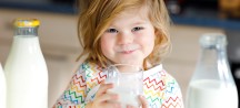 Mädchen sitzt lächelnd, mit einem Glas Milch in der Hand.
