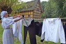 Das Foto zeigt eine Frau in historischer Kleidung, die Wäsche aufhängt