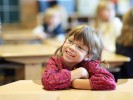 Ein kleines Mädchen sitzt an einem Arbeitstisch in der Schule und lächelt. Foto: Harald Oppermann