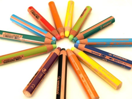 Buntstifte aller Farben liegen kreisförmig mit der Spitze in der Kreismitte.